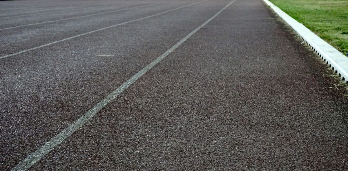 Detailed view of an empty athletic running track lane with visible surface texture and grass edge.